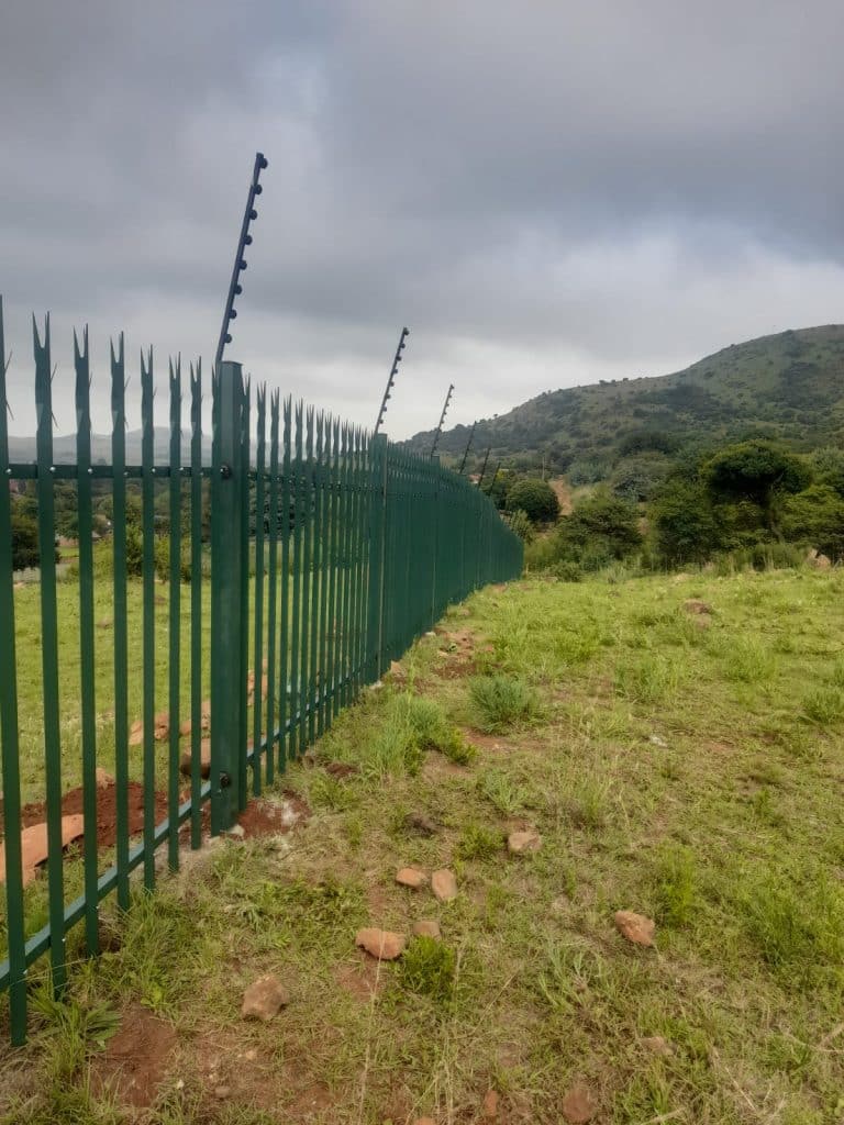 Green palisade security fence with electric top strands installed along a Gauteng hillside